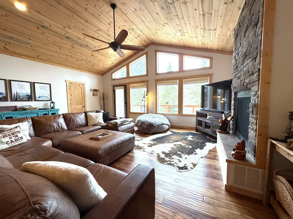 Cabin living room with double-sided gas fireplace and tall windows overlooking the forest